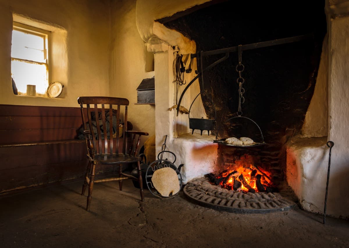 A wooden chair in a vintage style kitchen, with tools and fireplace for cook.