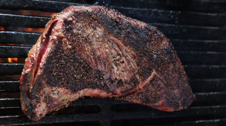 A nicely seared tri-tip steak sitting on a grill.