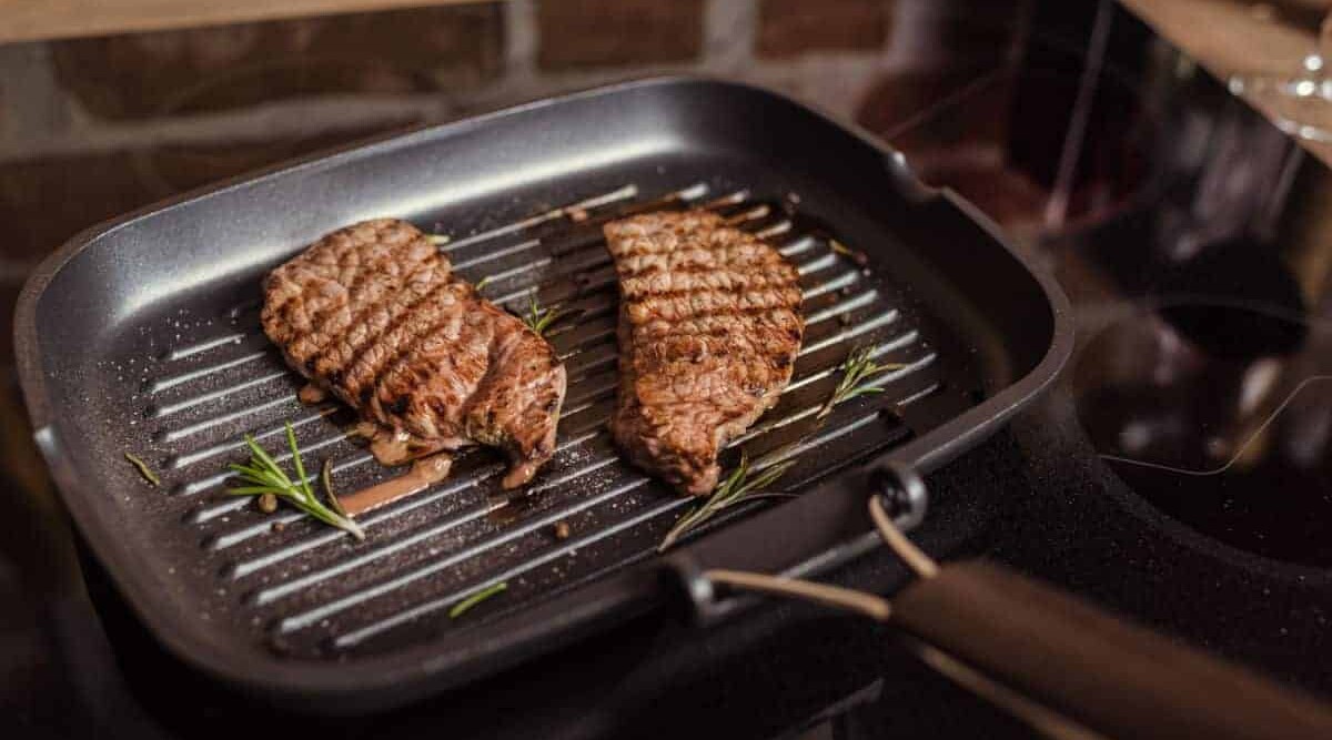 Close up of grilling indoors 2 steaks in a skillet.