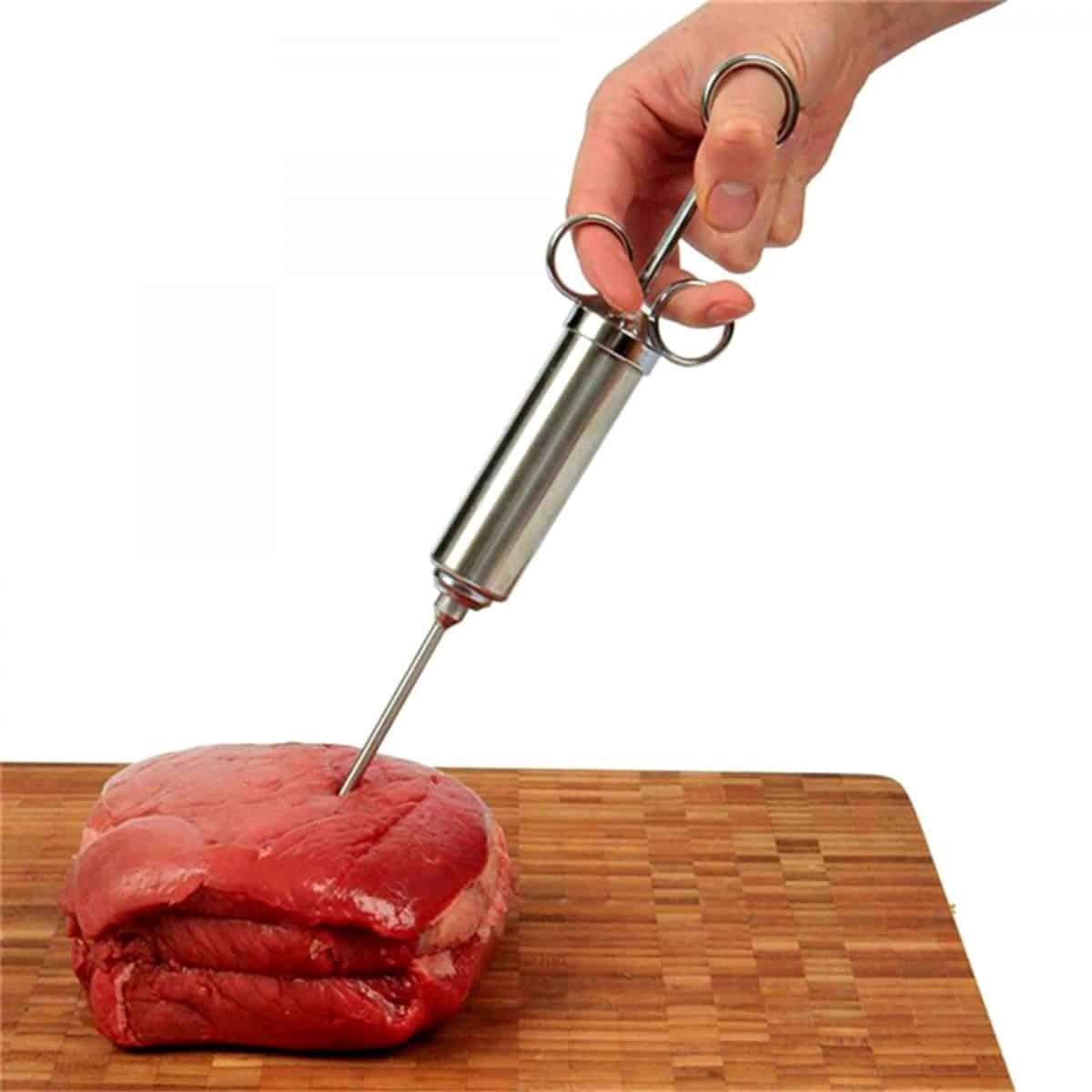 A hand injecting marinade into beef on a cutting board, isolated on white