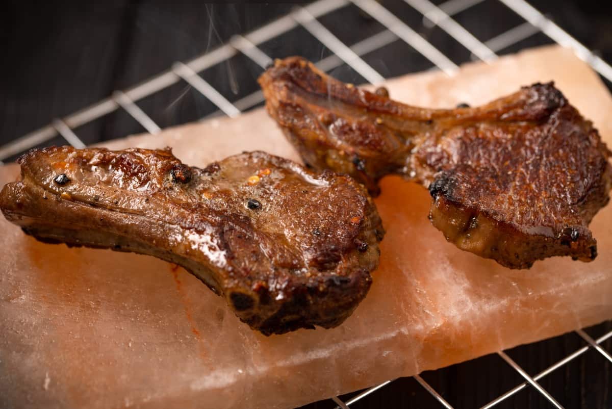 Two lamb chops grilling on a Himalayan salt bl.