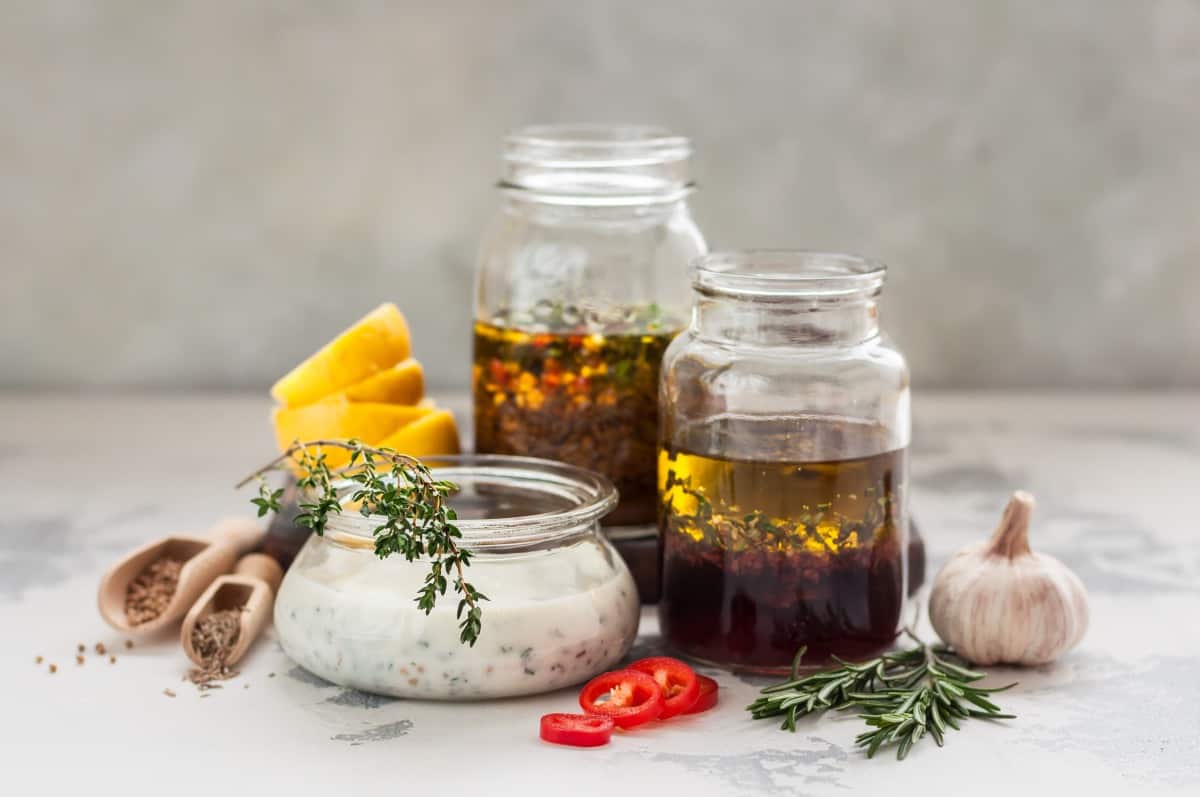 An assortment of 3 meat marinades in clear jars on a ta.