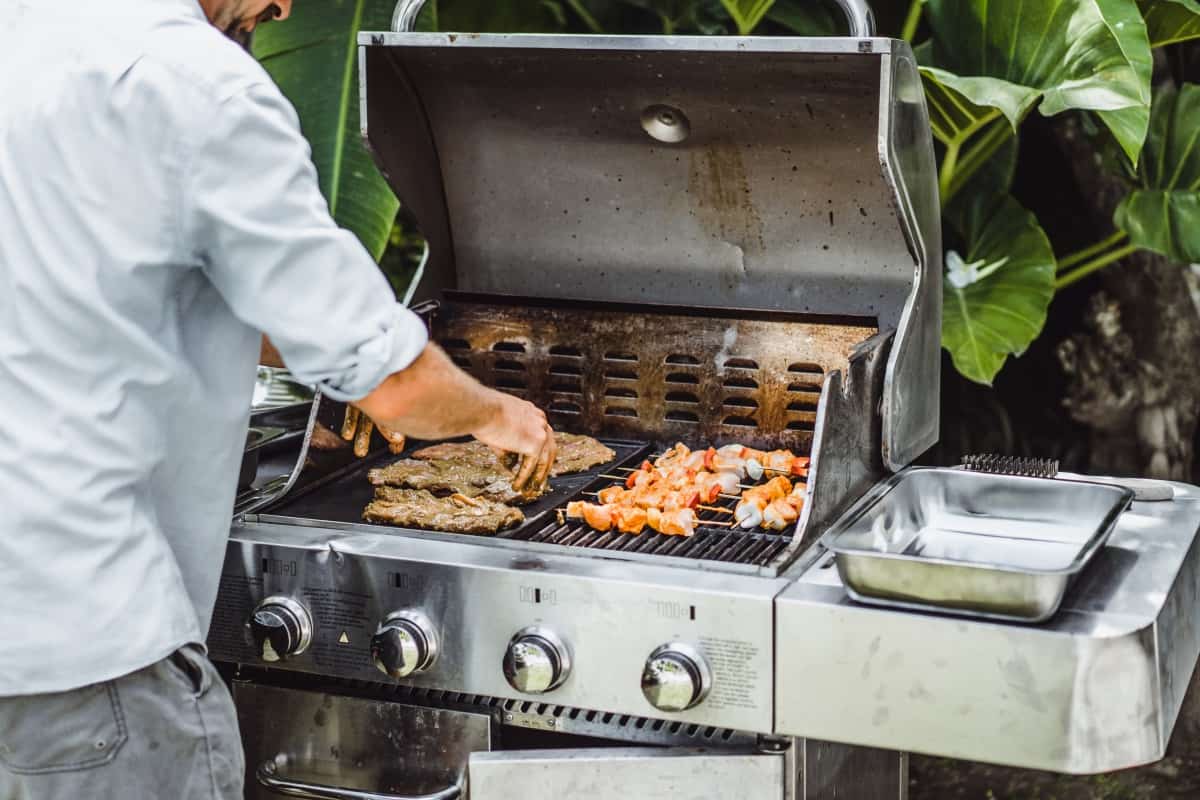 A man grilling meat on a gas gr.