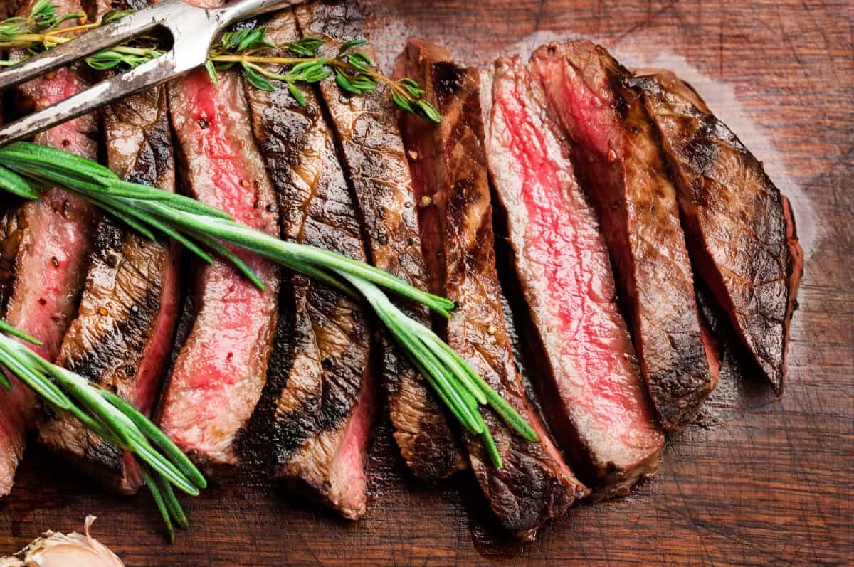 Medium rare grilled flank steak, sliced, with a rosemary and a thyme sprig resting on .