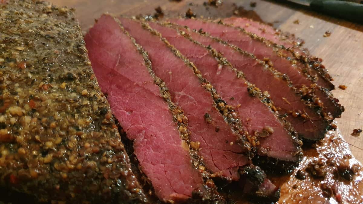  Dark pink sliced pastrami with a pepper crust on a cutting bo.