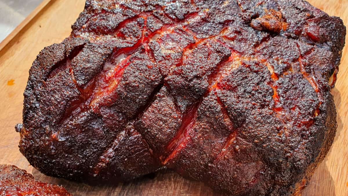 A smoked pork butt with crisscross scoring on a cutting bo.