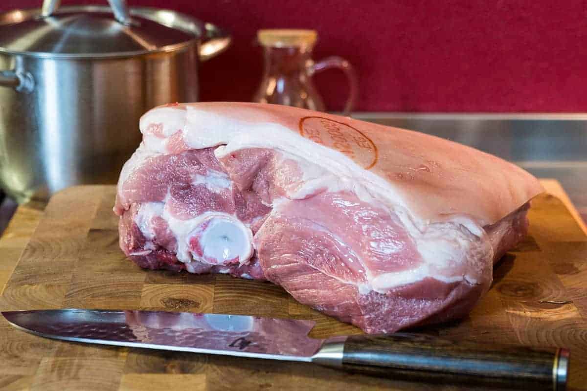 Close up of a pork butt, fat side up, on a wooden chopping board with a kitchen knife in