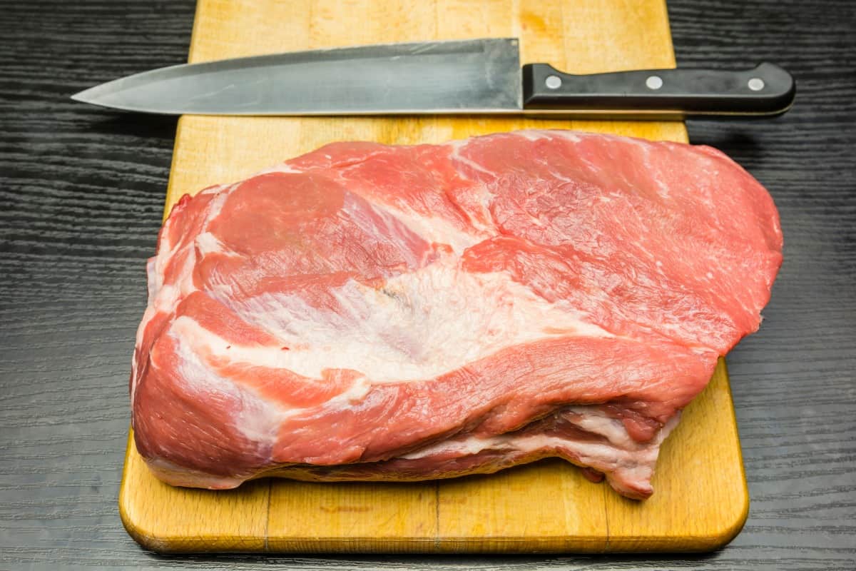 A raw pork butt on a cutting bo.