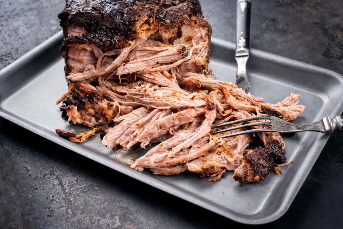 Pulled pork on a metal serving tray, being ripped with a fork