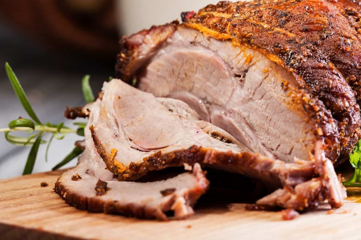 roast pork shoulder with the end sliced on a cutting bo.