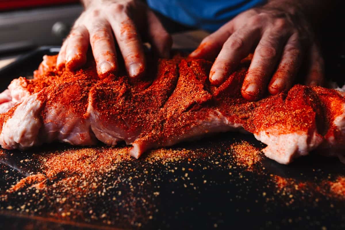 A mans hands rubbing meat with a bright red spice .