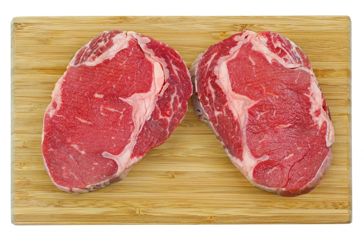 Two select ribeye steaks on a wooden cutting bo.