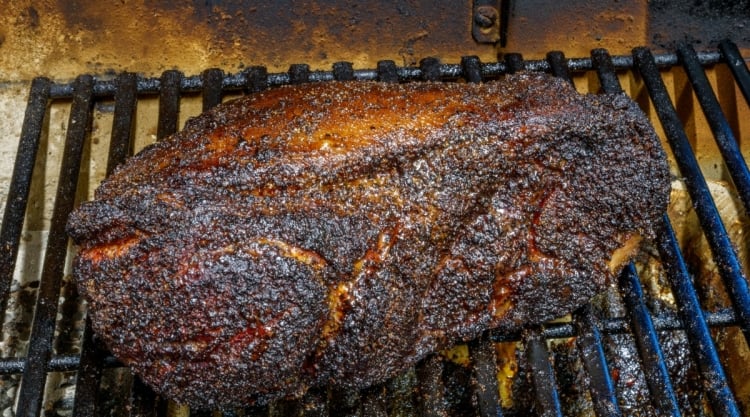 A well rubbed pork shoulder with a dark crust sitting in a smoker
