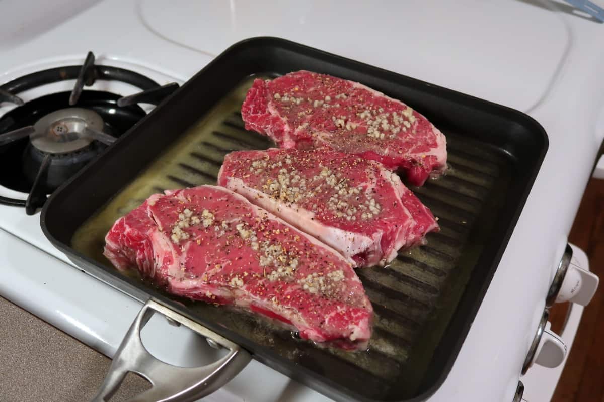 Three steaks cooking on a stovetop gr.