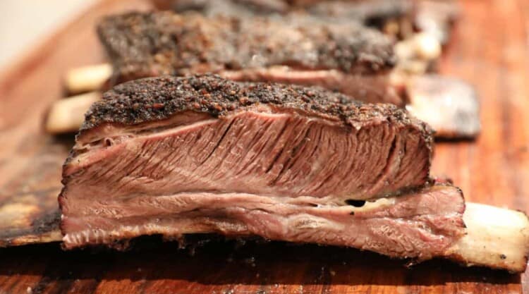 Close up of some smoked beef short ribs on a wooden chopping board.