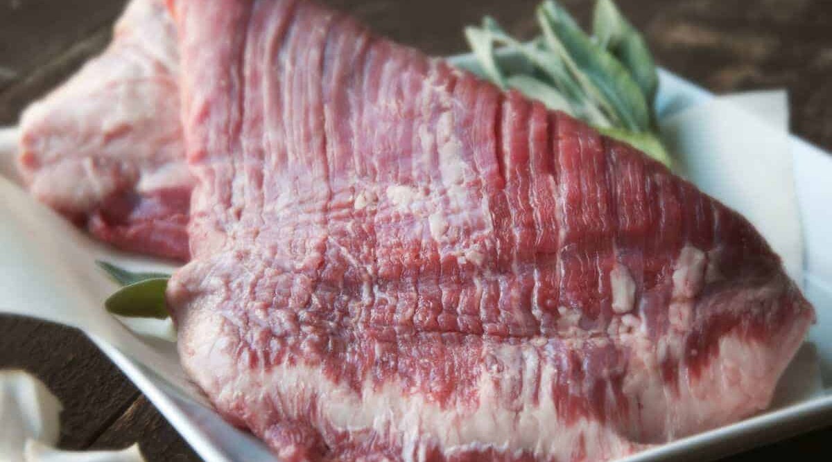 Close up of some flank steak in ceramic cookware with some rosemary.