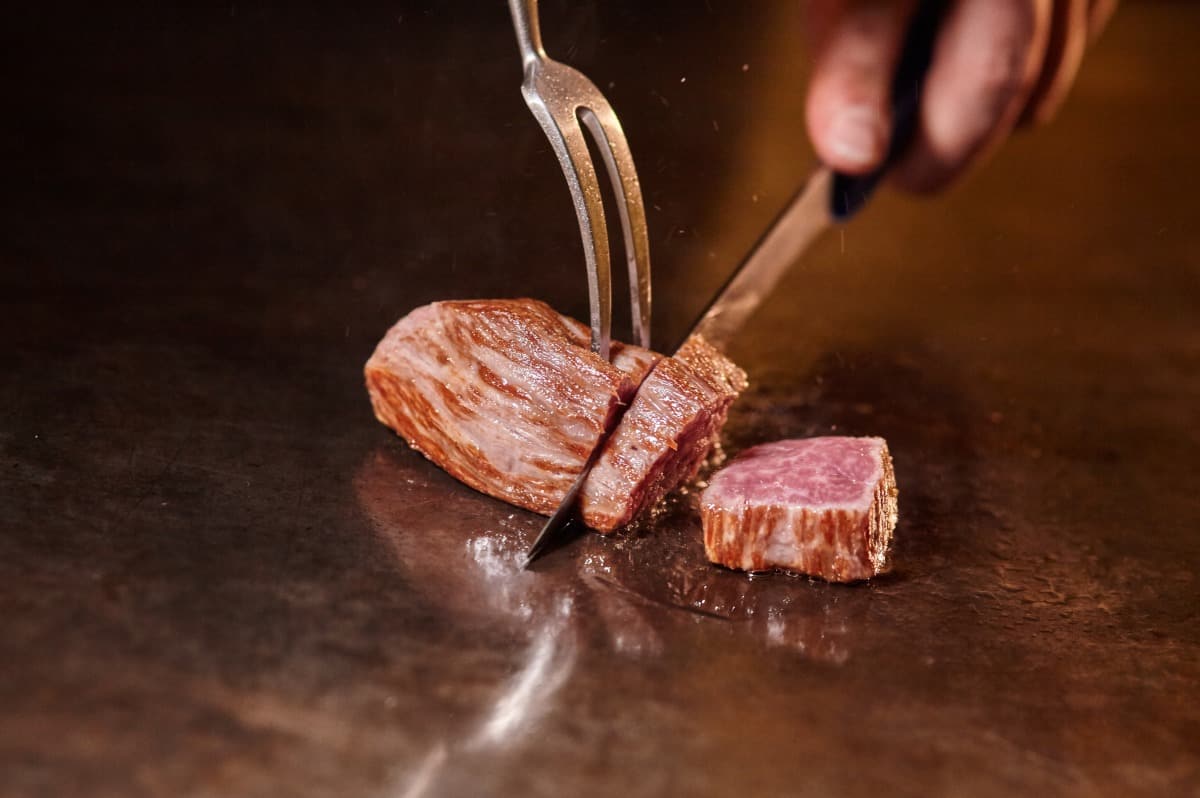 A chef hand cooking wagyu on a hot plate, with a knife and fork