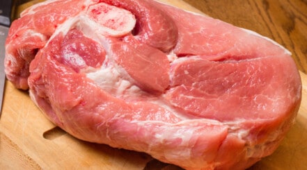 Close up of a pork butt, showing the money muscle, sitting on a wooden chopping board.