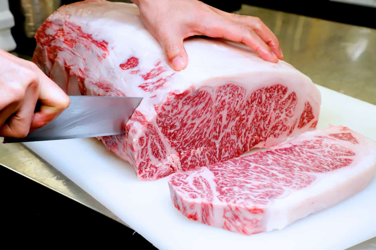 A large wagyu beef joint being sliced into steaks by a c.