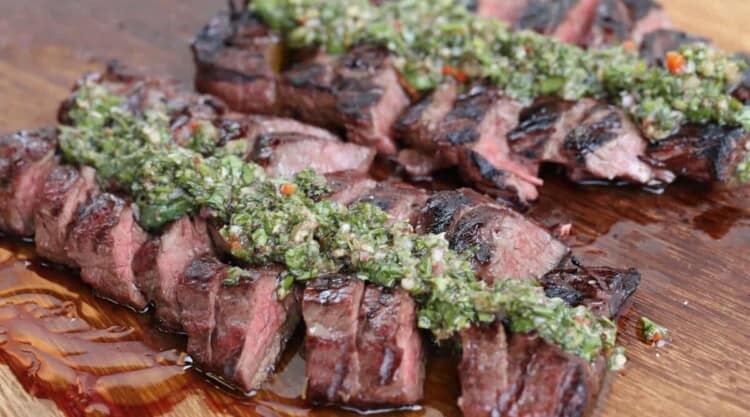 Grilled, sliced hanger steak with chimichurri on a large wooden chopping board