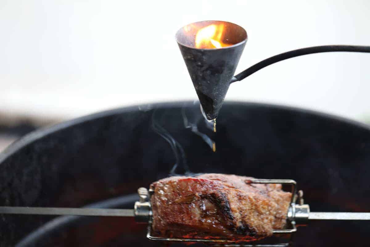 A flambadou dripping flaming fat onto a sirloin roast on a rotisse.