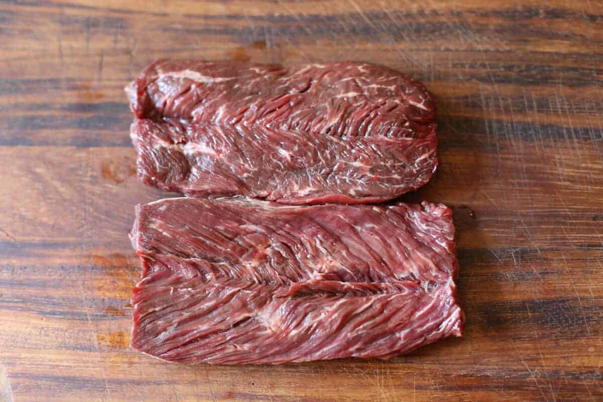 overhead view of 2 raw hanger steaks on a large wooden chopping board