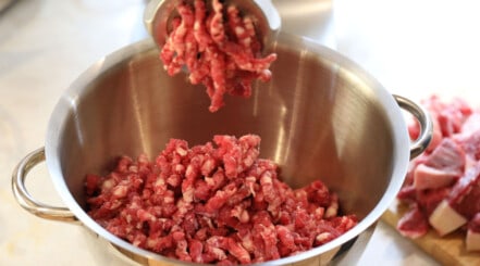 Close up of an electric meat grinder being used to grind beef for burgers