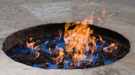 A gas fire pit sunken into a stone table, with orange flames licking out above the rim.