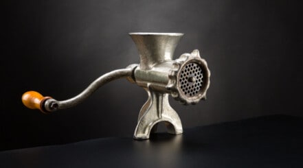 A manual meat grinder isolated against a black background.
