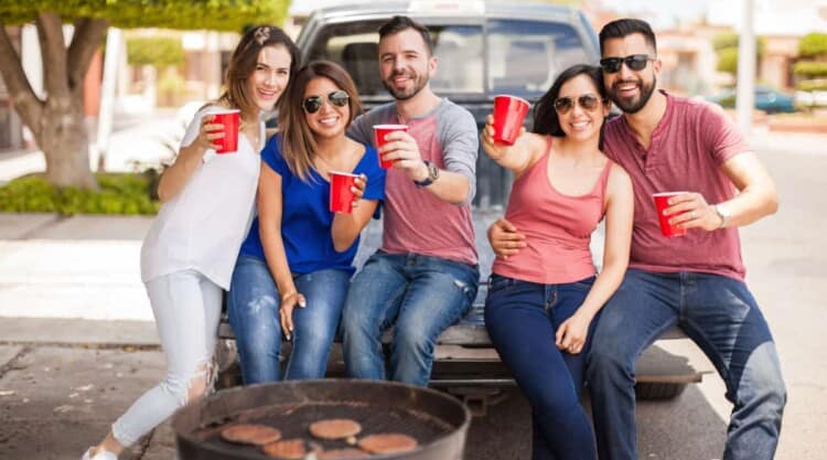 A group of friends tailgating, grilling and drinking from red cups.