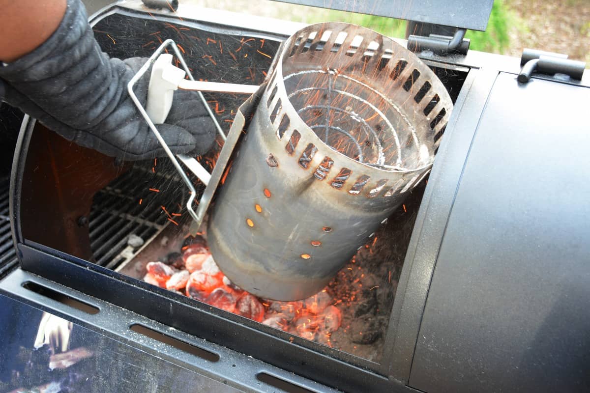 A charcoal smoker being filled with lit coals from a chimney star.