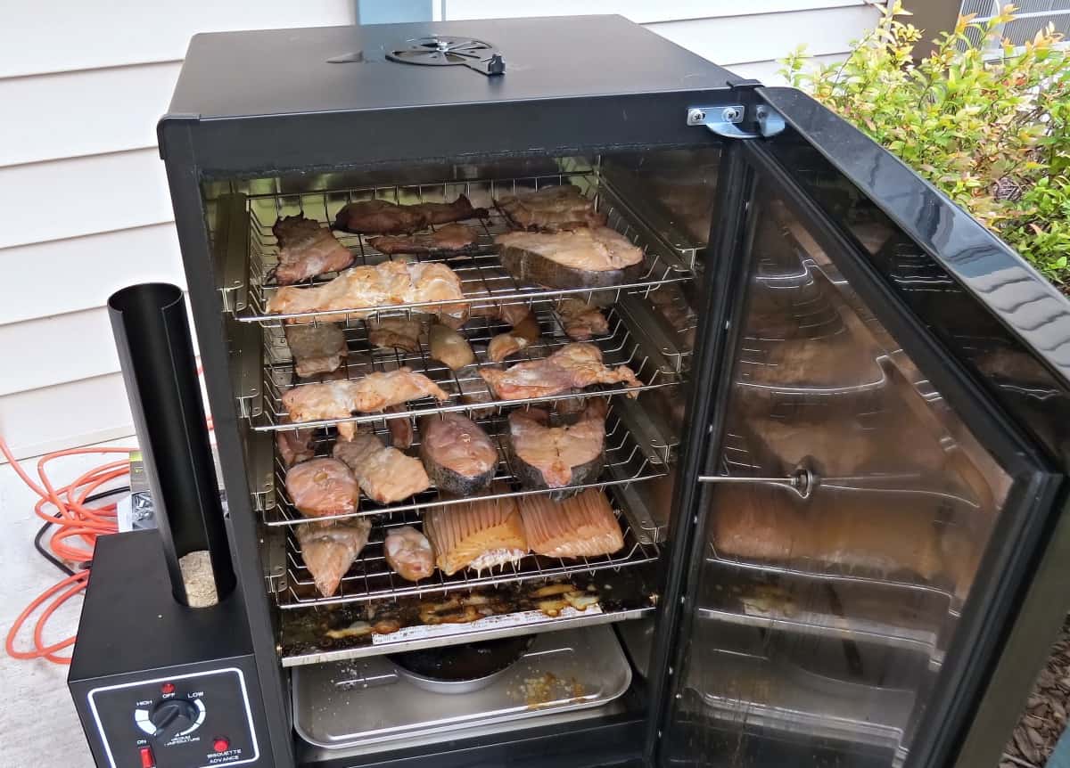 An electric smoker, door open, and it fully loaded with meat and f.