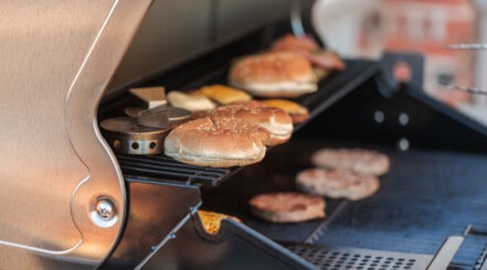 Beefburgers cooking on a gas grill outdoors.