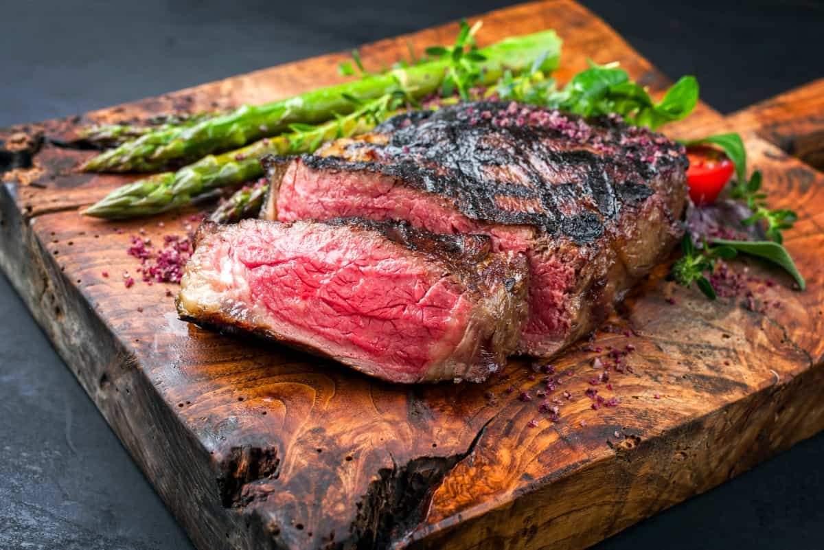 A grilled, sliced, medium rare steak on a cutting board with asparag.