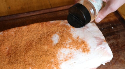 A mans hand liberally sprinkling dry rub over pork ribs.