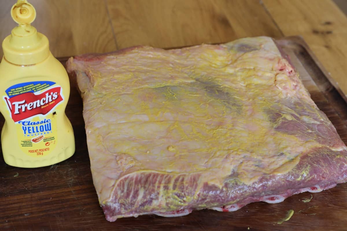 Pork rubbed in mustard, next to a bottle of french's mustard