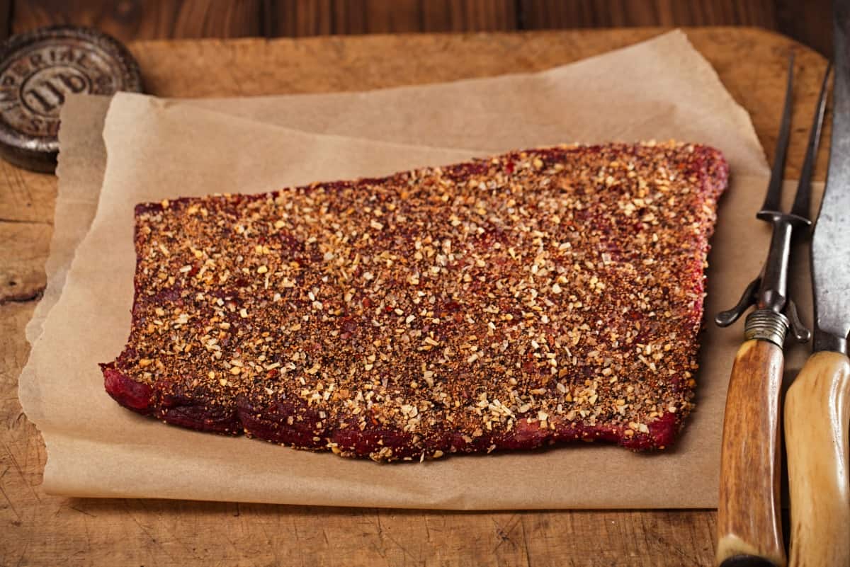  Dry rubbed beef on a cutting board with a fork and slicing kn.