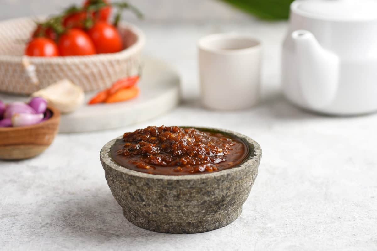 A bowl full of wet rub, with tomatoes, herbs and spices in the backgro.