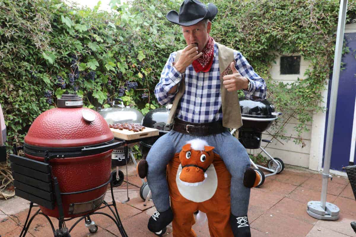 A man in fancy dress eating ABTs next to a red Kamado Joe gr.