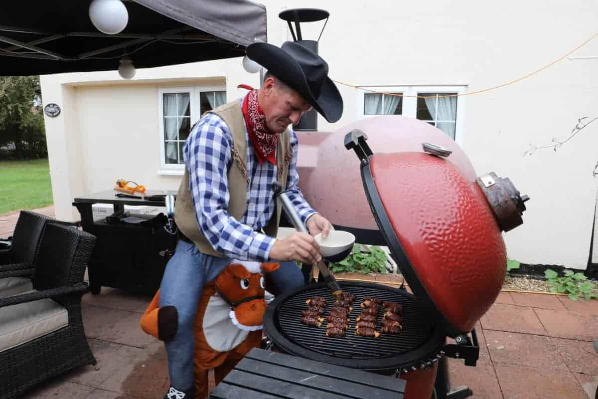 A man in fancy dress adding BBQ sauce to ABTs on a kamado gr.