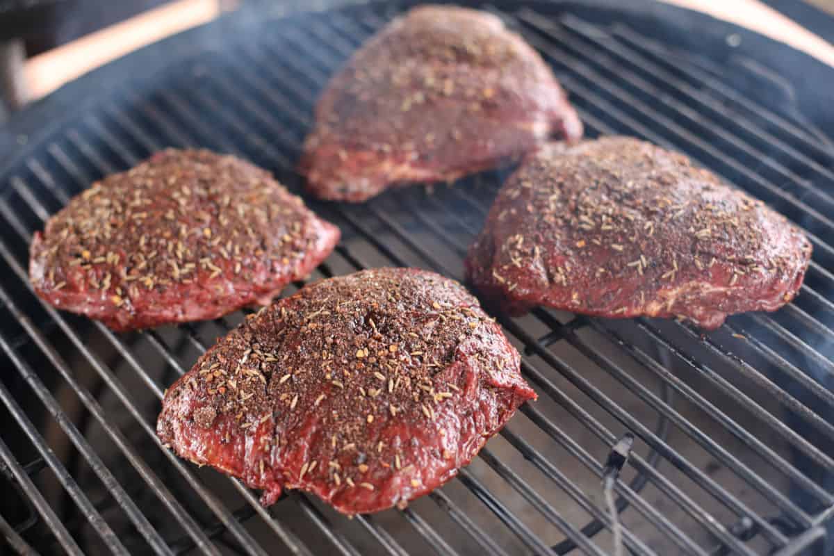 Four beef cheeks with a herby dry rub, sitting inside a kamado smo.