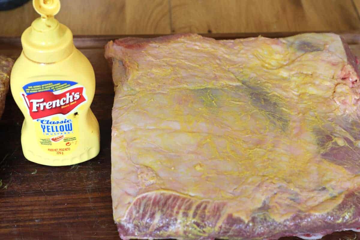 Rack of beef ribs lightly covered in mustard, next to a bottle of French's mustard