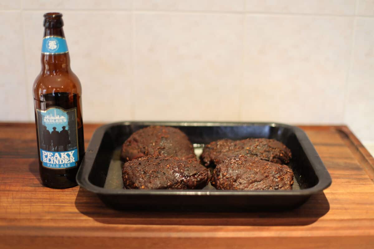 Four beef cheeks in a pan next to a bottle of .