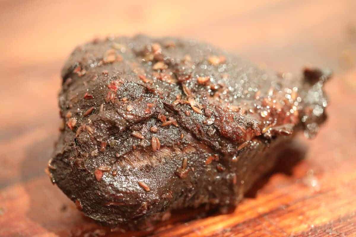 Fully cooked beef cheek on a wooden chopping bo.