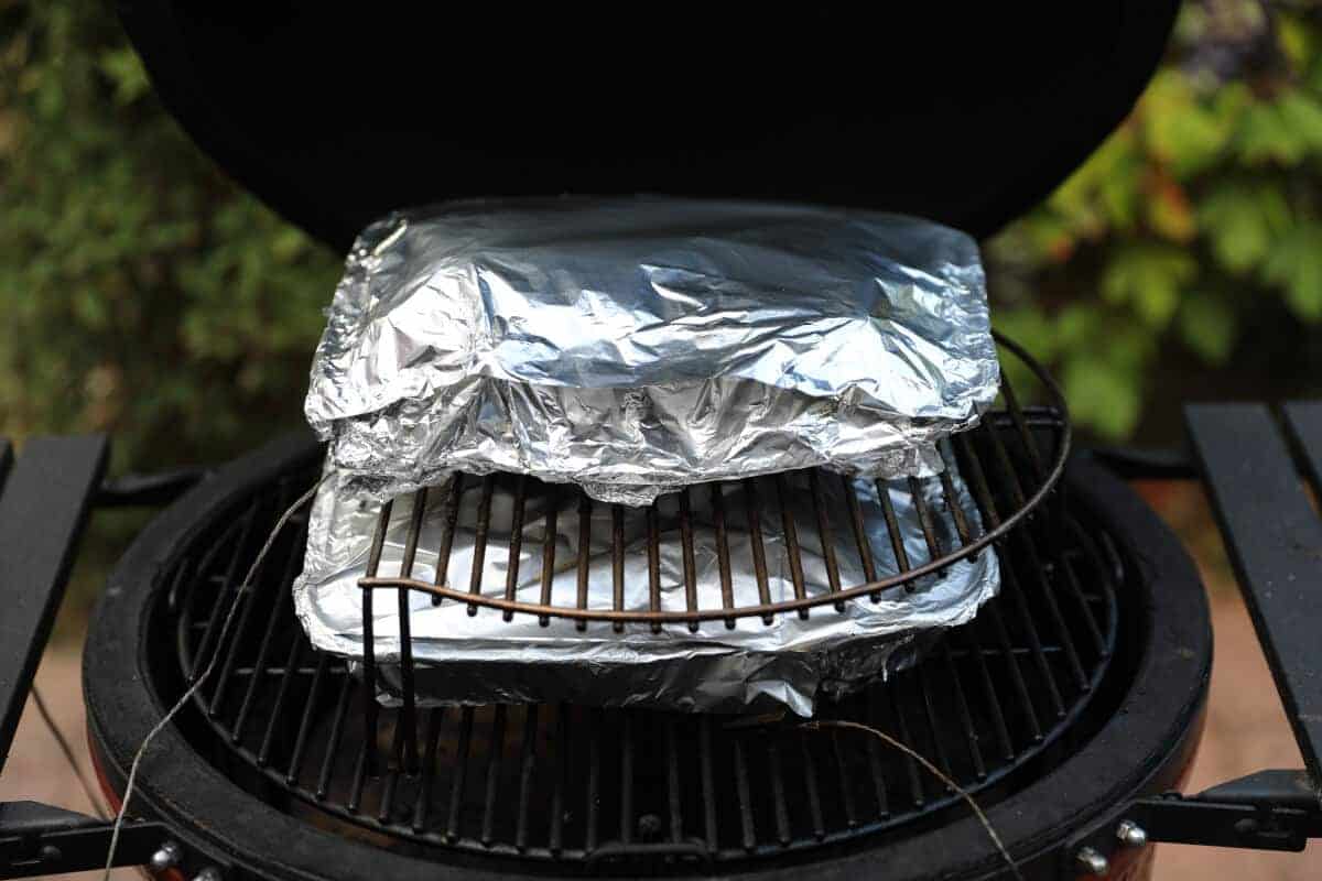 Beef ribs wrapped in aluminum foil on a Kamado Joe smo.