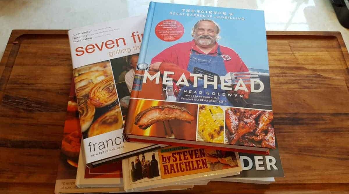 Some of the best BBQ and grilling cookbooks piled on each other on a table.