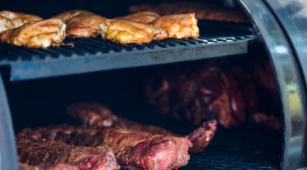 Close up of a selection of meat in a two-tier BBQ smoker.