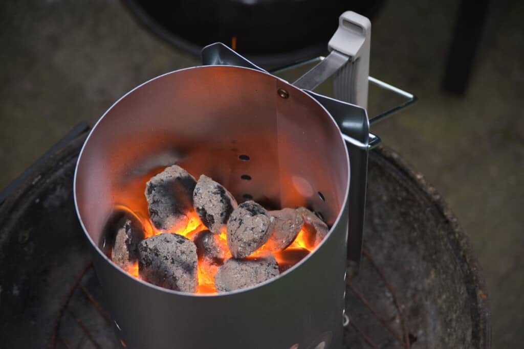 A charcoal chimney starter half full of hot burning coals