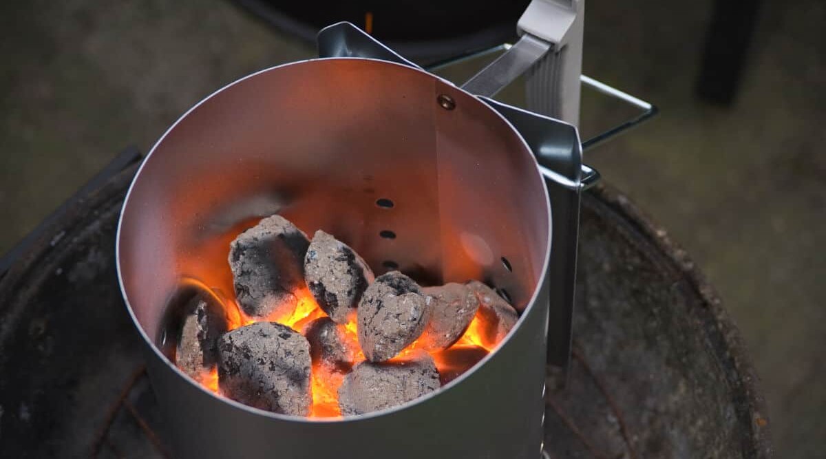 A charcoal chimney starter half full of hot burning coals.