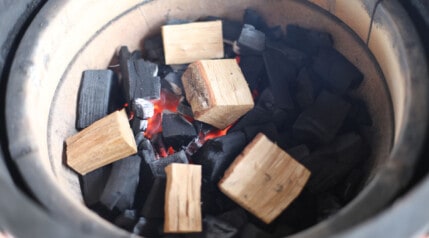 Close up of a Kamado Joe fire bowl filled with lump charcoal and smoking wood.